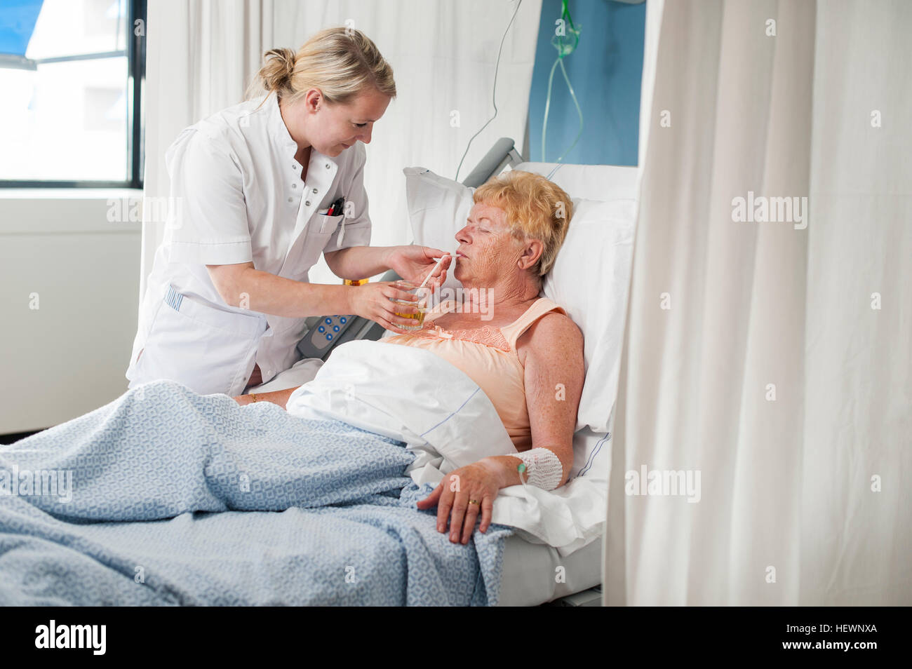 Nurse helping patient in hospital bed take a drink Stock Photo
