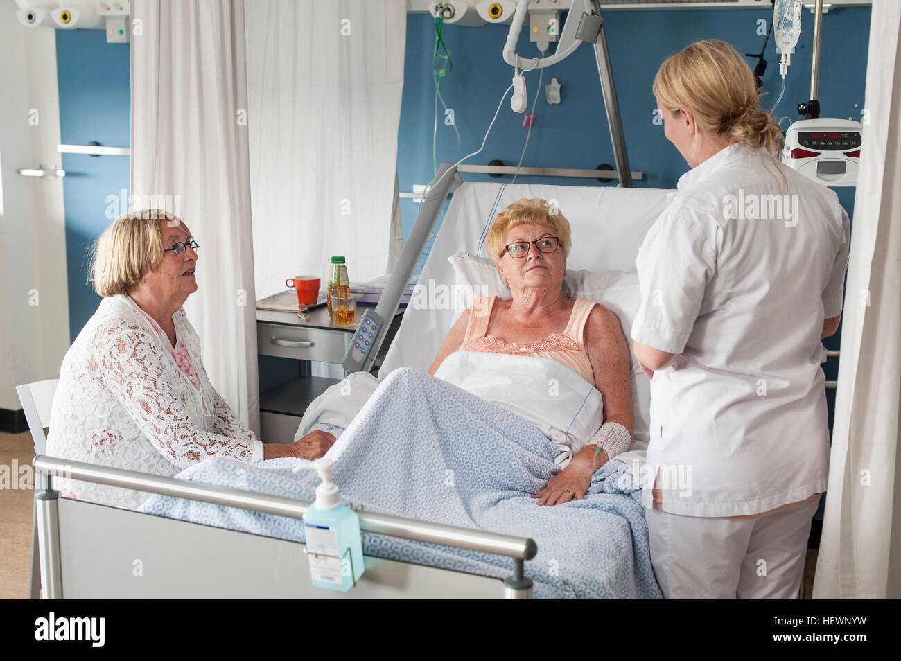 Nurse and visitor tending to patient in hospital bed Stock Photo