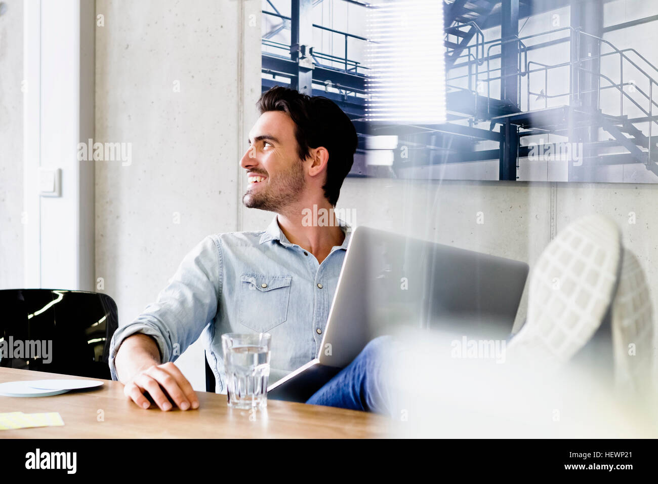 Business man in office feet up on desk, using laptop looking away smiling Stock Photo