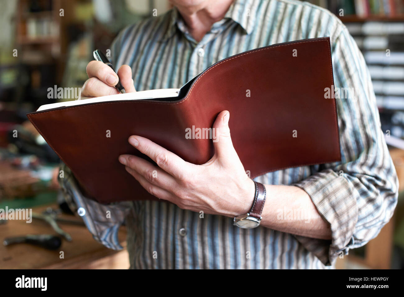 Man in leather workshop, writing in leather bound notebook, mid section, close-up Stock Photo