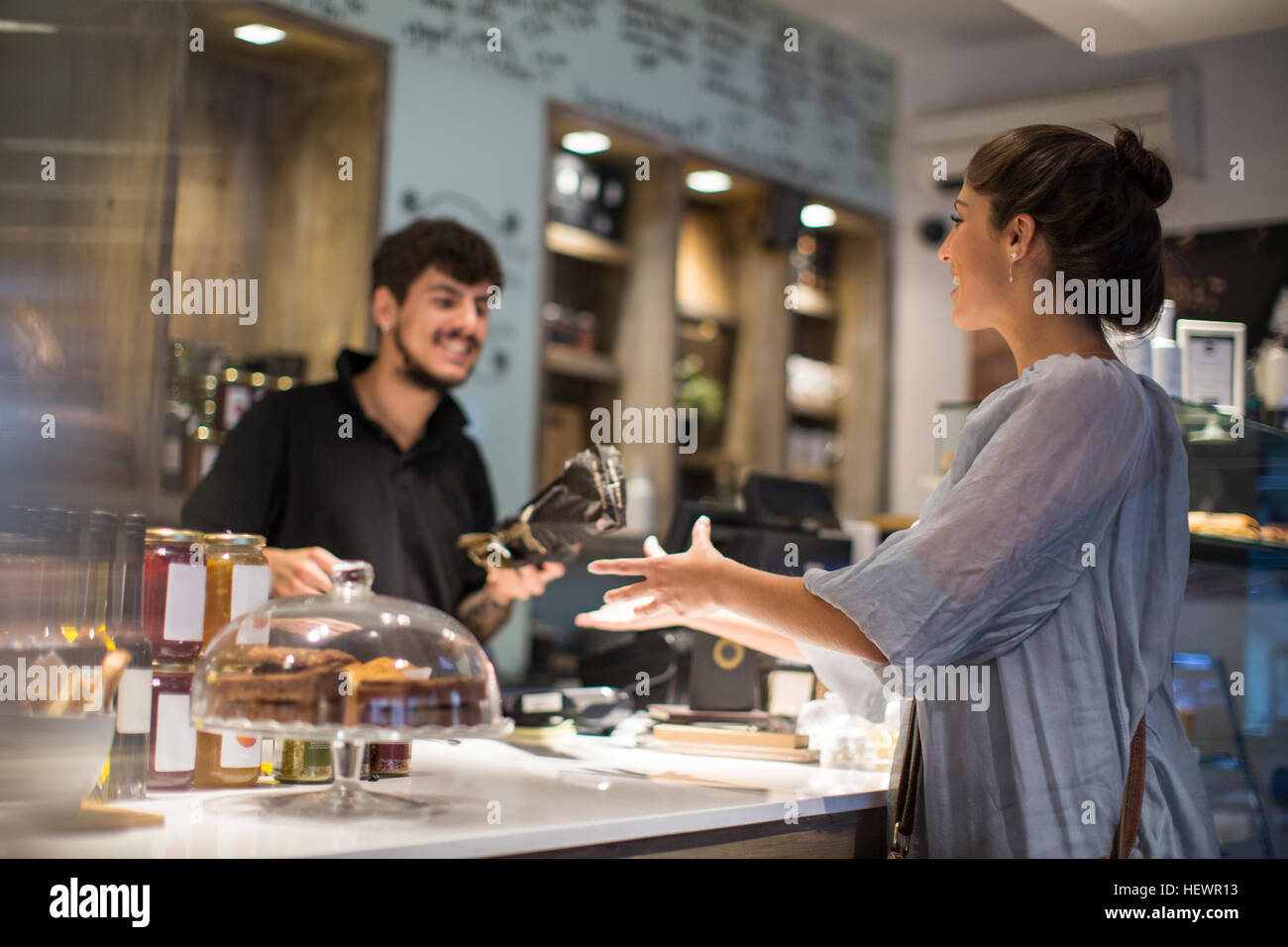 Barista handing baguette to female customer at cafe counter Stock Photo
