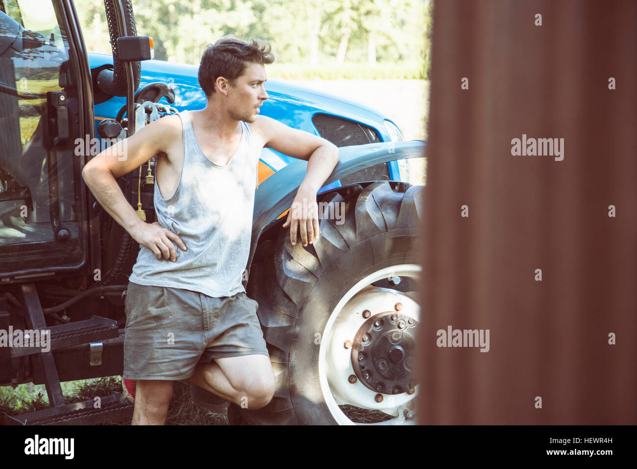 Young male farmworker leaning against tractor Stock Photo
