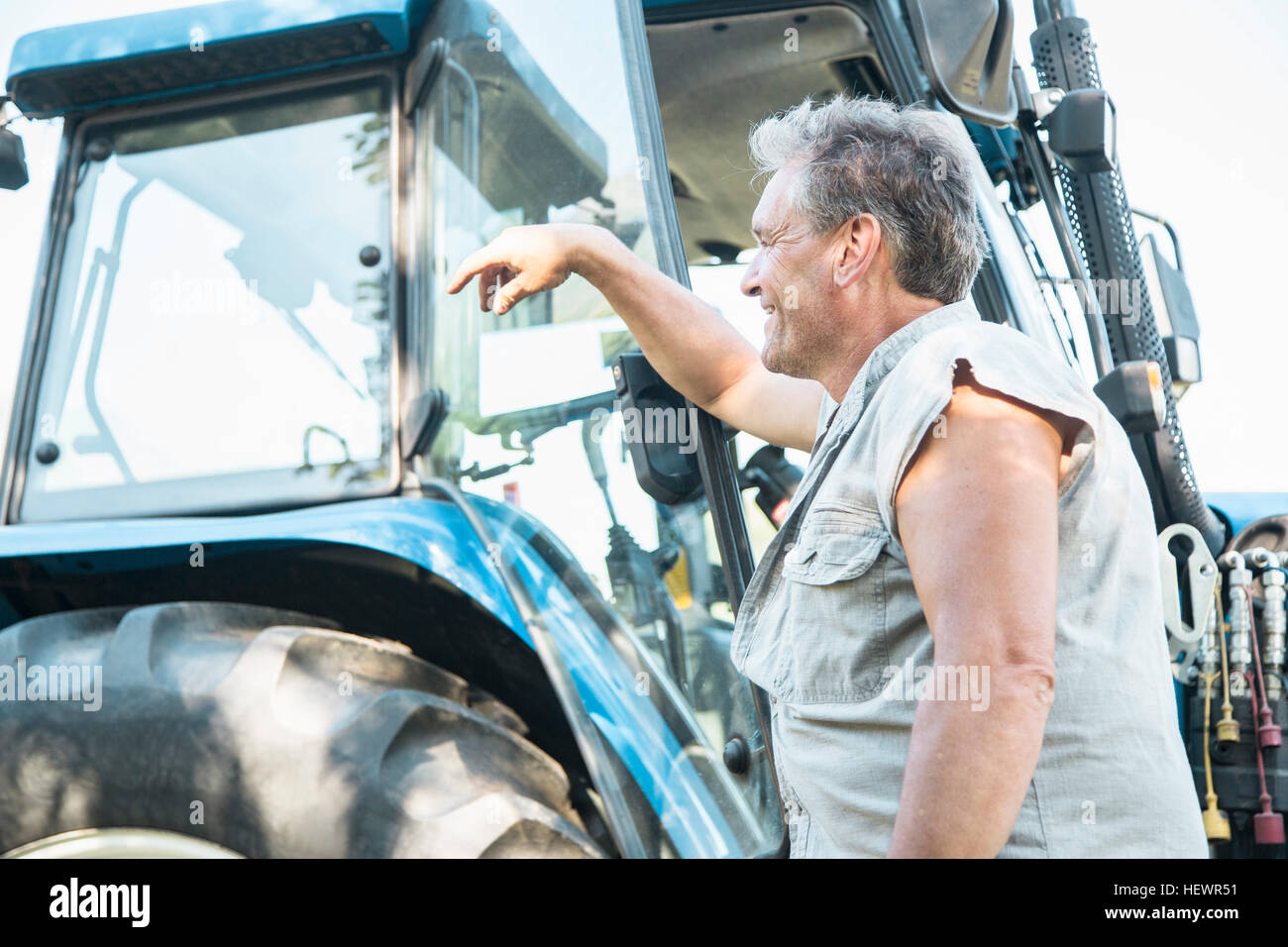 Mature male farmworker leaning against tractor Stock Photo