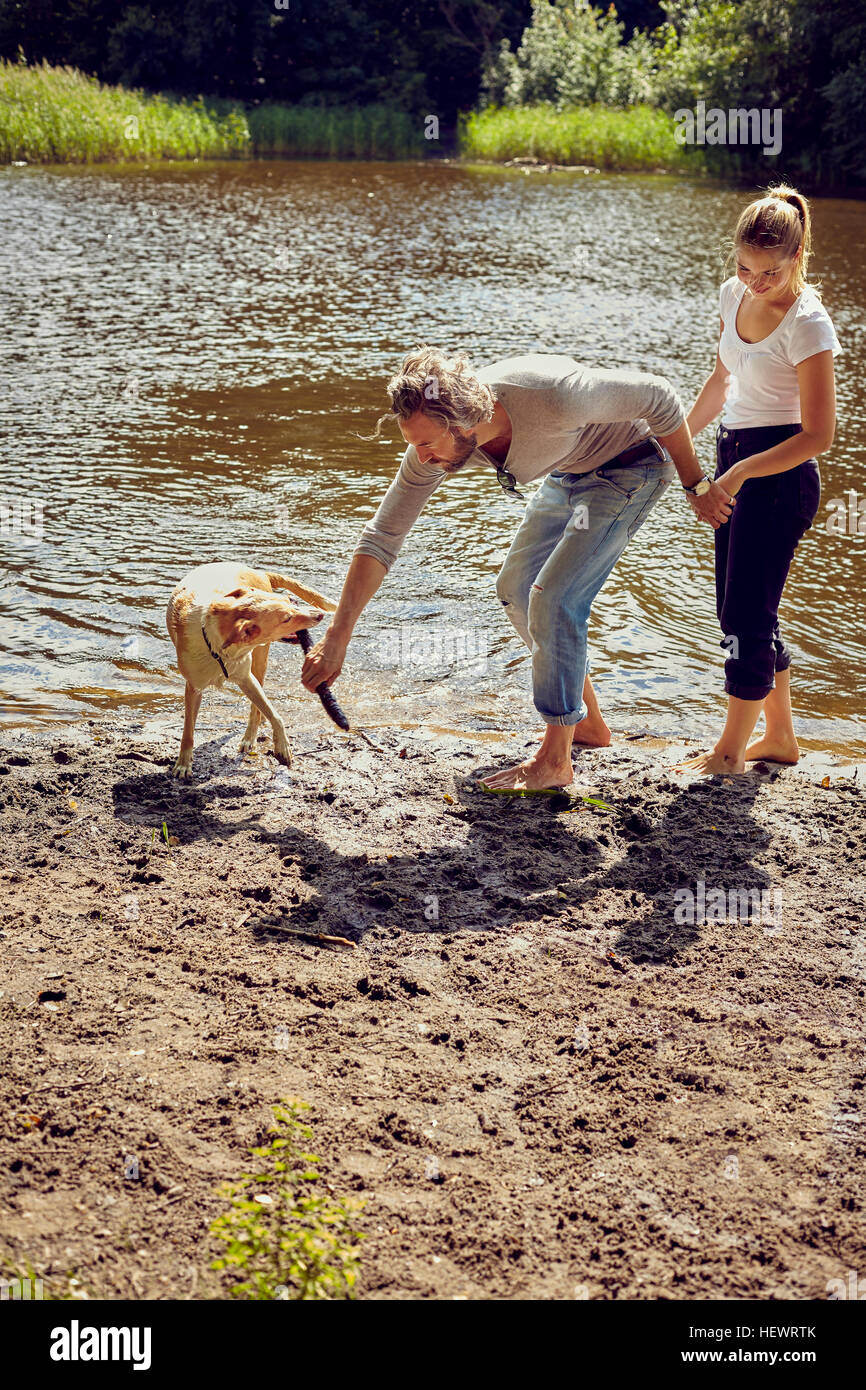 Couple playing with dog on riverside Stock Photo - Alamy