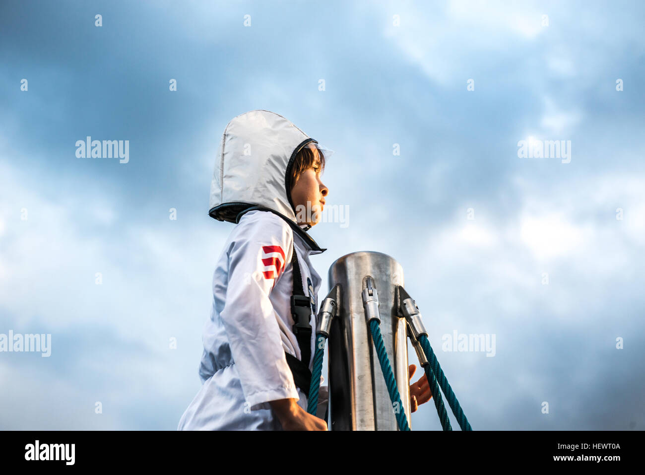 Portrait of boy in astronaut costume gazing out from top of climbing frame against dramatic sky Stock Photo