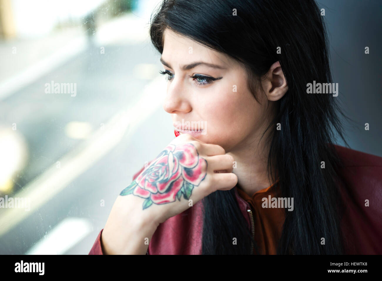 Young woman with tattoo on hand, looking through window Stock Photo