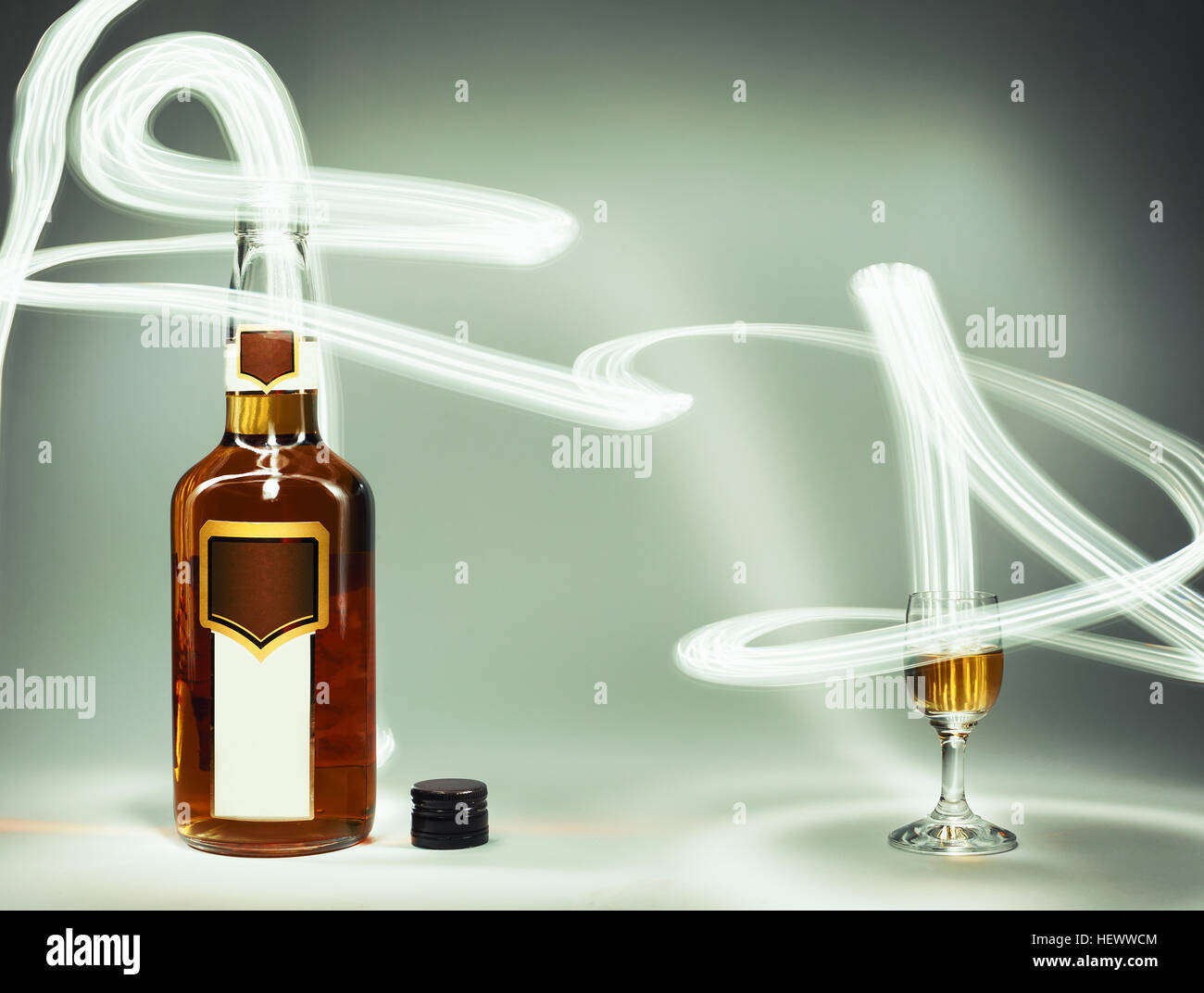 Conceptual composition of alcoholic drinks, full brandy bottle and a glass and lighting effects. Stock Photo