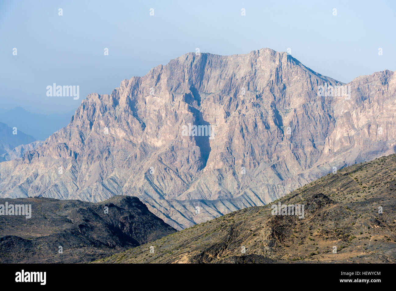 The steep slopes of arid jagged mountains overlooking an eroded and inhospitable rocky desert valley. Stock Photo