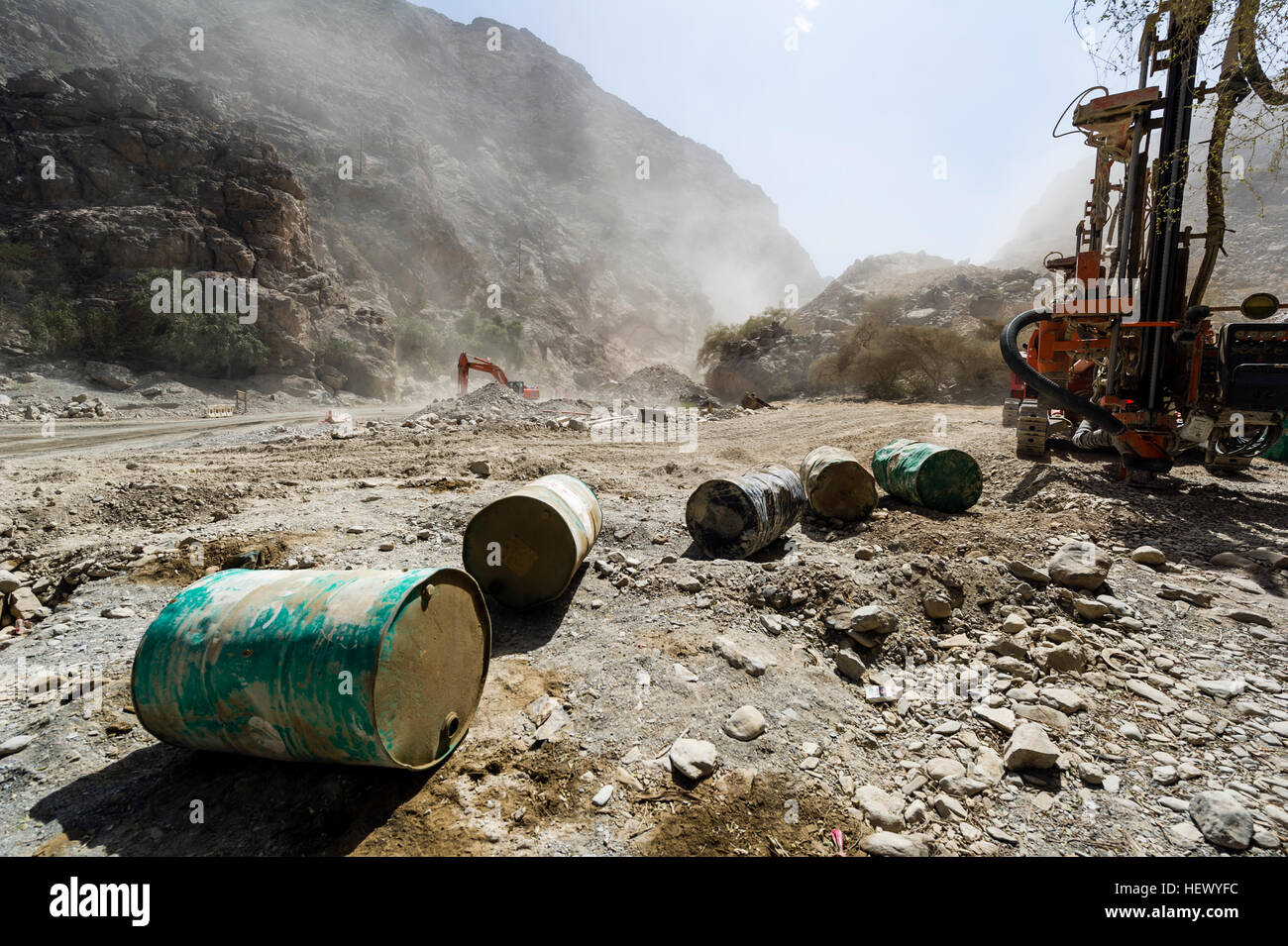 Oil drums and road construction machinery in a dusty desert gorge. Stock Photo