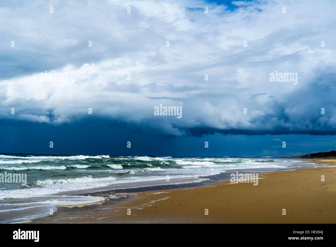 Ominous black storm clouds roll in over waves rolling onto an empty beach. Stock Photo