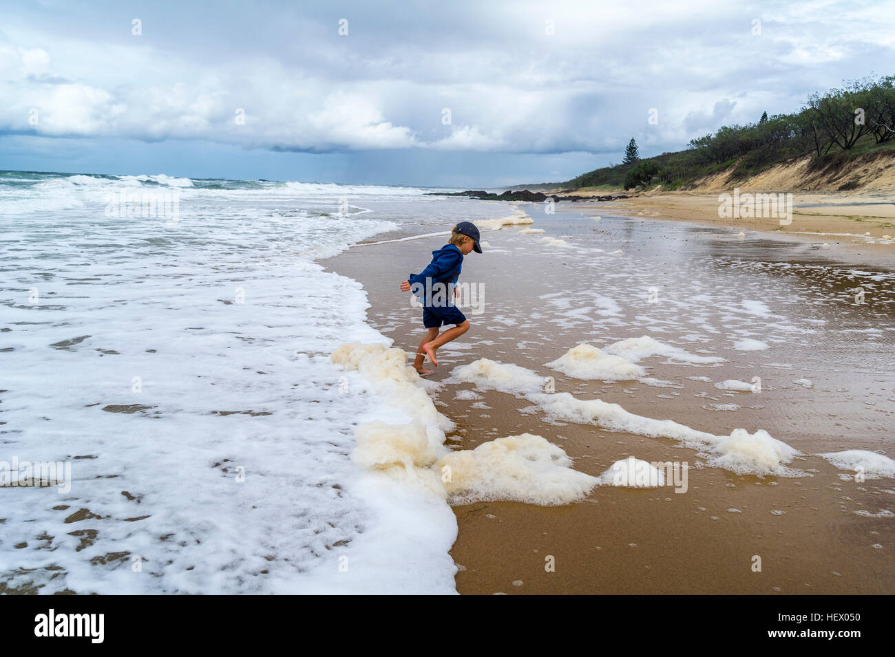 A boy playing in the shallows as storm surge waves roll onto an empty beach. Stock Photo