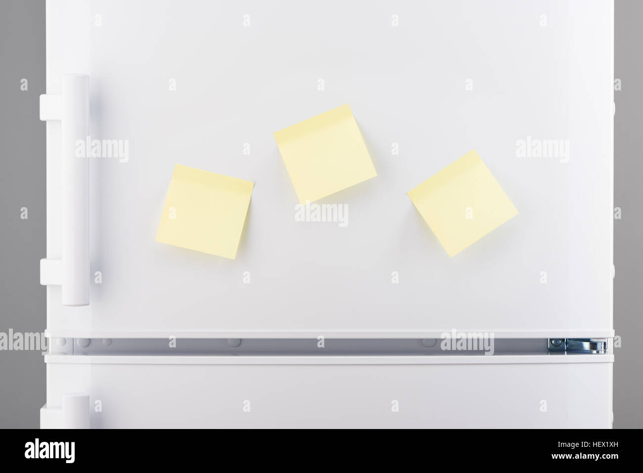 Three blank light yellow sticky paper notes on white refrigerator door Stock Photo