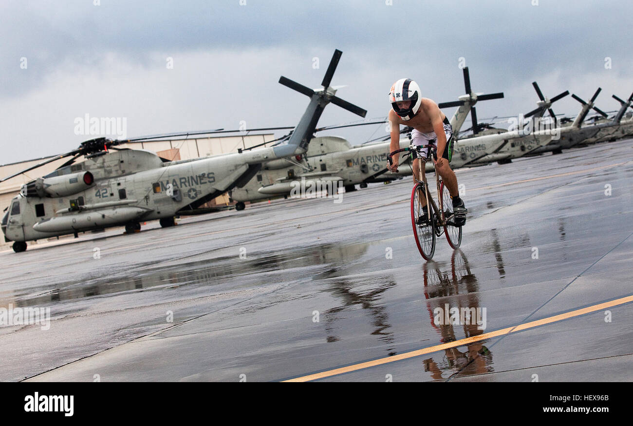 A competitor bicycles past a row of helicopters while laboring through the 11.1-mile bicycle course during the 2011 Sprint Triathlon outside Hangar 101 on Marine Corps Base Hawaii, May 22, 2011. Comprised of a 500-meter swim, 11.1-mile bike race and a 5-kilometer run, the triathlon was the first of two in the 2011 Commanding Officer’s Fitness Series. The event was hosted by Headquarters Battalion and Marine Corps Community Services Semper Fit division. Triathlon competitor races past CH-53's at MCB Hawaii Stock Photo