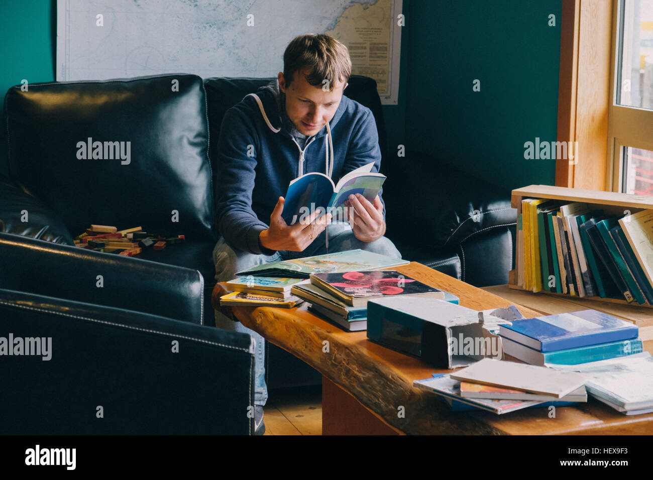Mid adult man sitting in chair, looking through books Stock Photo