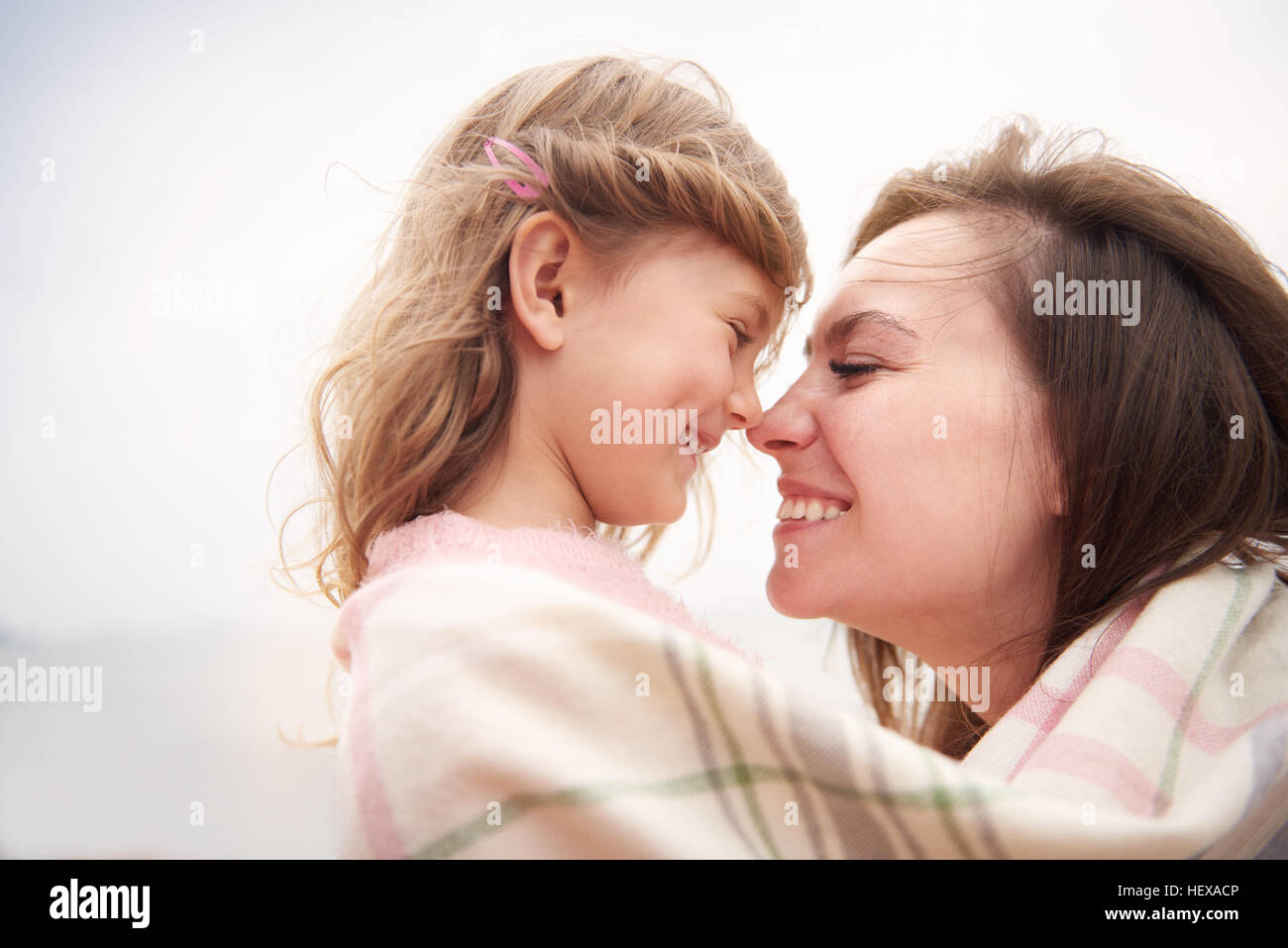 Happy mother and daughter wrapped in blanket, rubbing noses Stock Photo