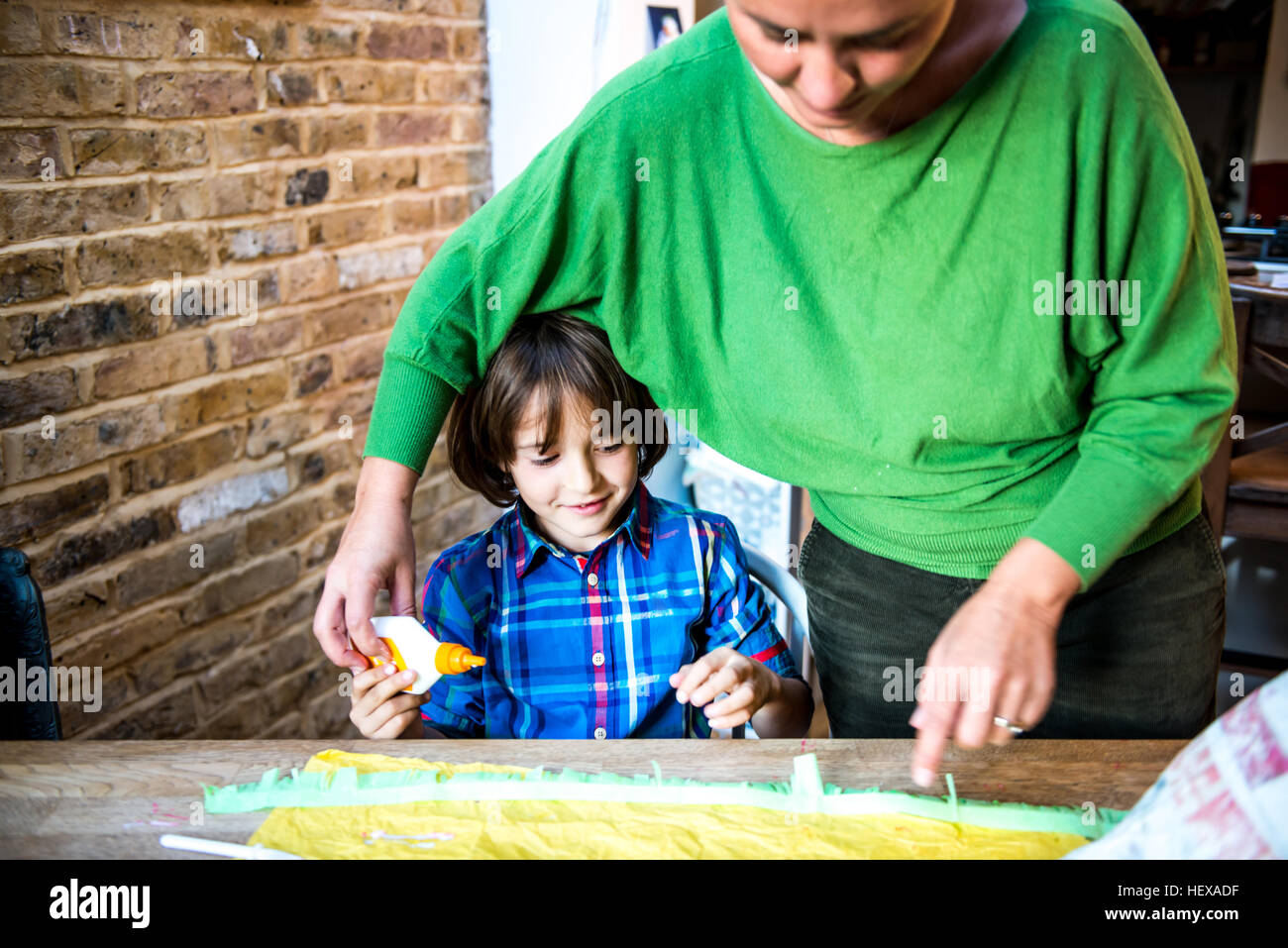 Mother helping son spread glue on crepe paper to make pinata Stock Photo