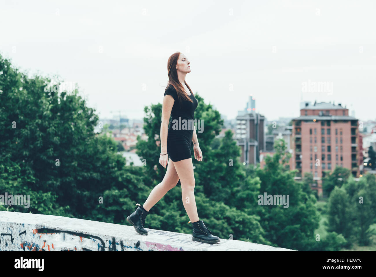 Young woman in mini dress walking on wall above city Stock Photo