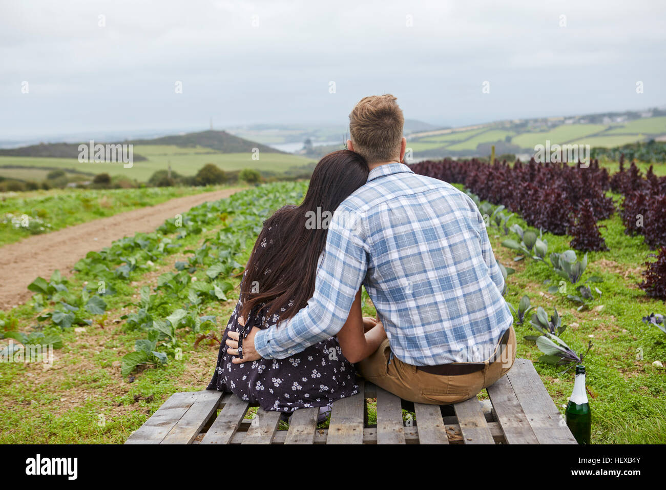 Couple in rural location sitting on pallets looking away Stock Photo