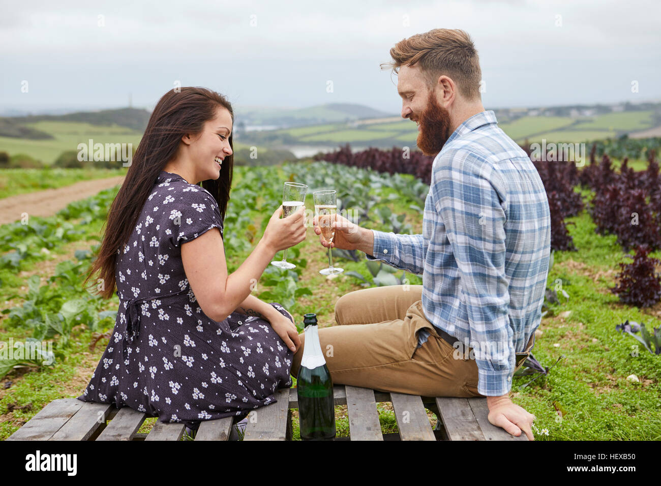 Couple in rural location sitting on pallets making a toast Stock Photo