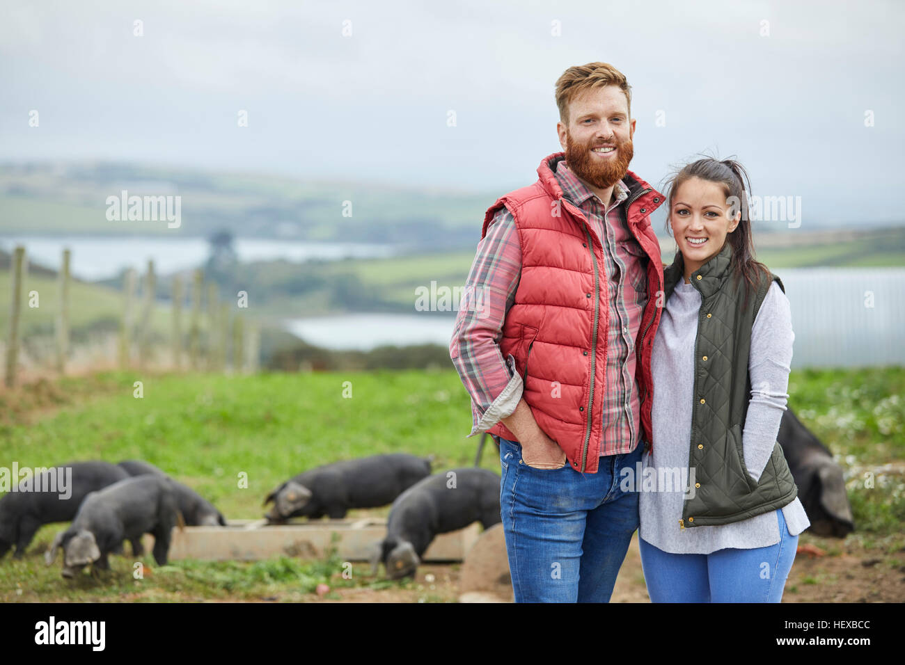 Couple on pig farm looking at camera smiling Stock Photo