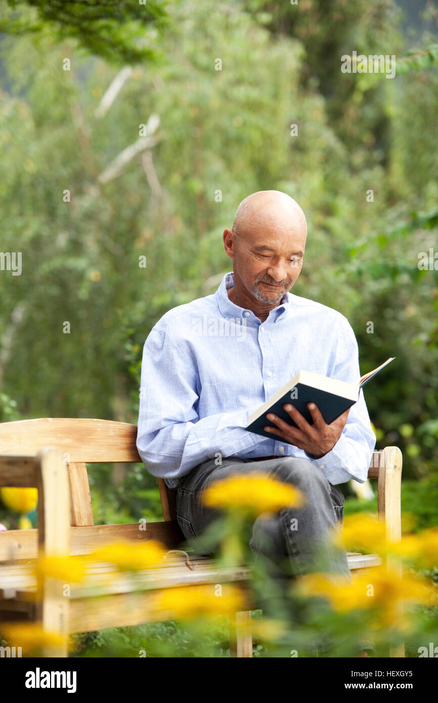Senior man sitting on garden bench reading book Stock Photo Alamy