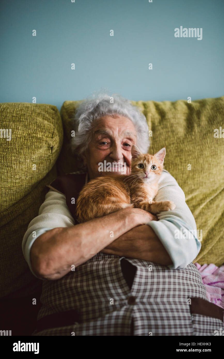 Portrait of happy senior woman cuddling with her cat on the couch Stock Photo