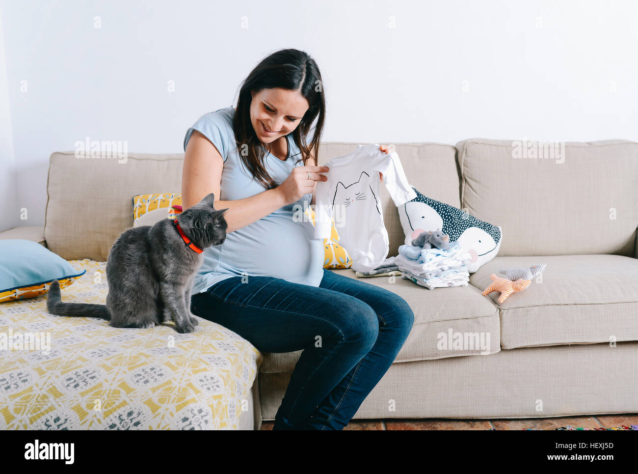 Pregnant Woman With Cat Sitting On Couch Looking At Baby Sleepers Stock Photo Alamy