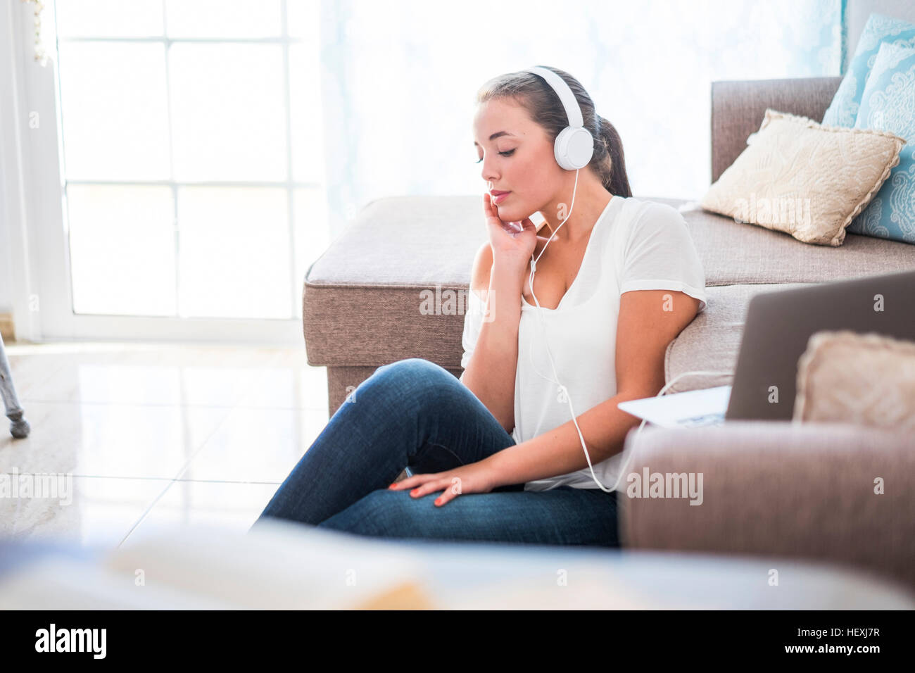 Young woman sitting on the floor of living room listening music with ...