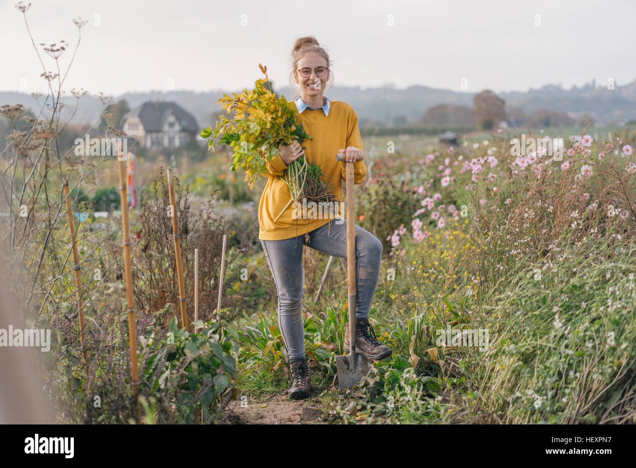Smiling young woman holding plant in cottage garden Stock Photo - Alamy