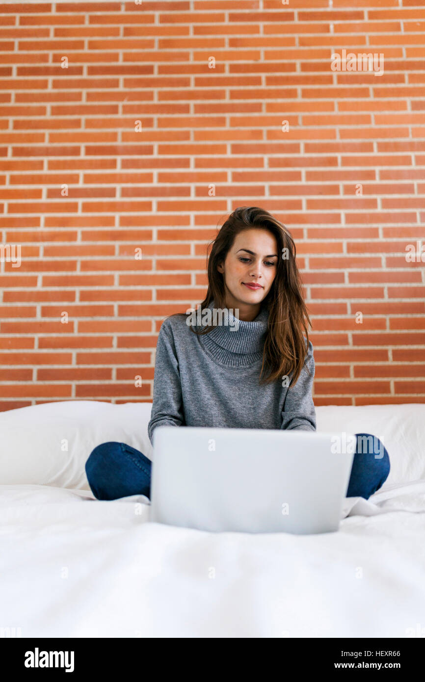 Young woman sitting on bed using laptop Stock Photo Alamy