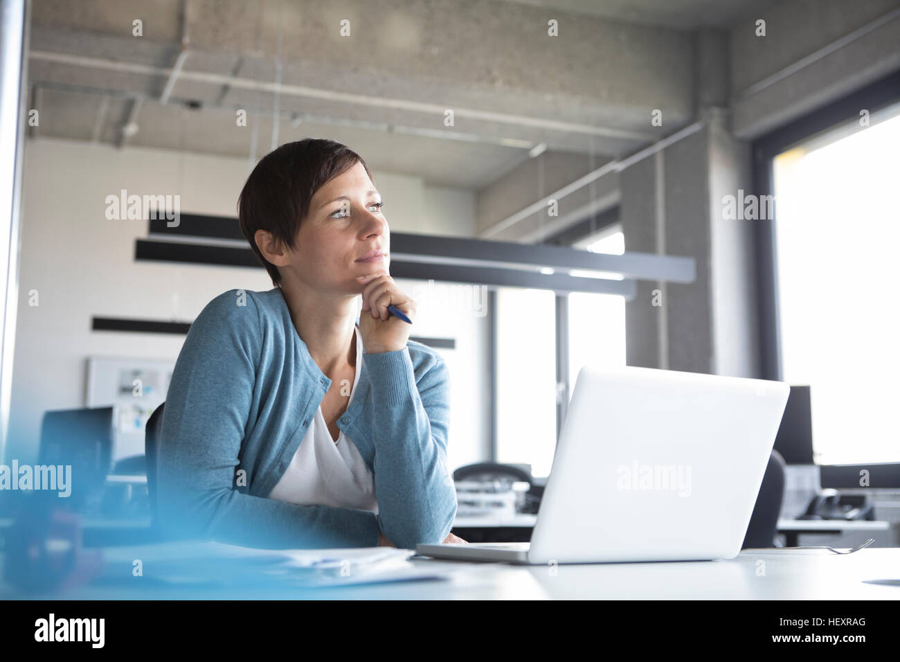 Businesswoman in office with laptop thinking Stock Photo