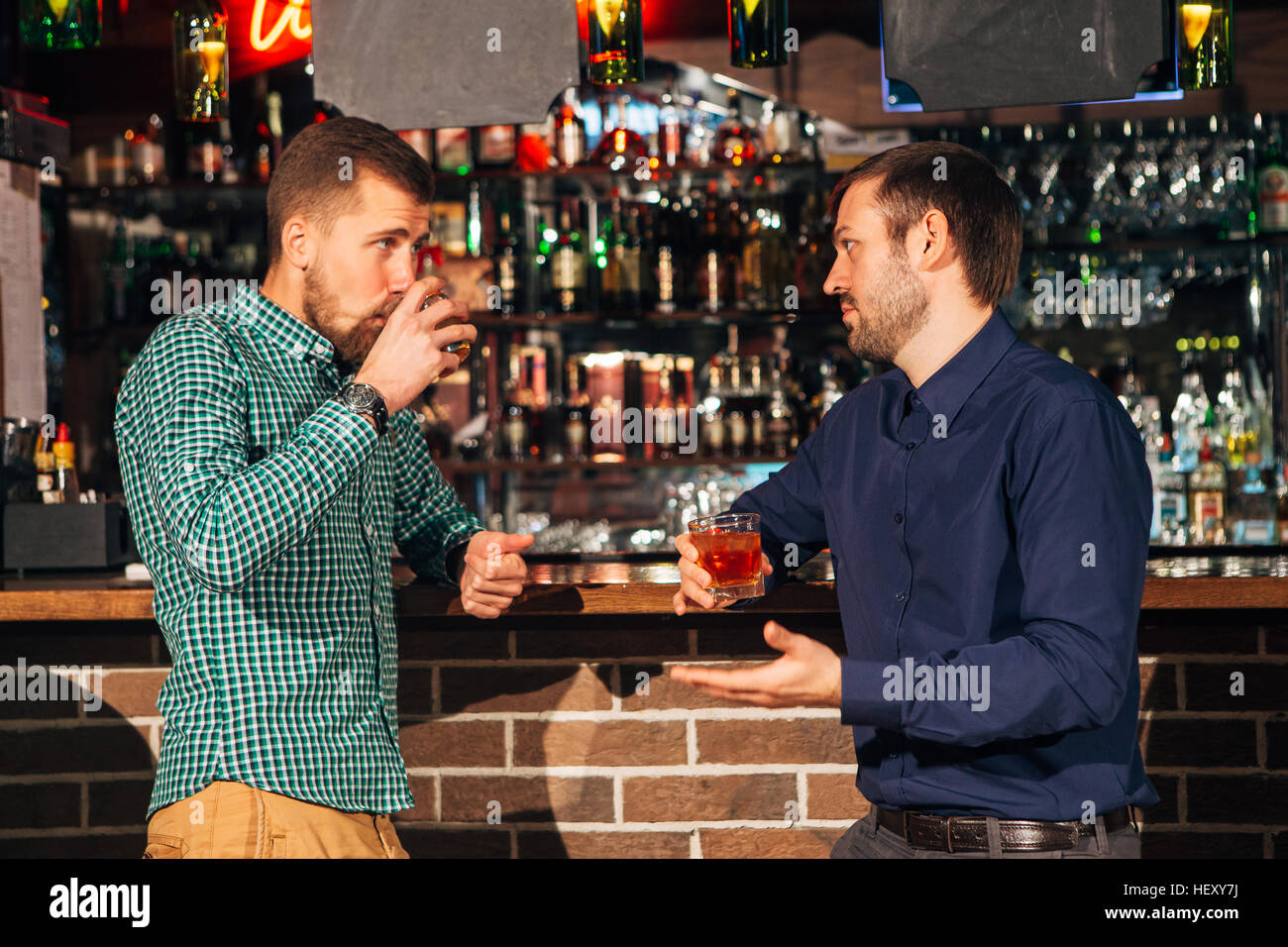 two young man talking at counter.  friends standing in bar and drinking whisky Stock Photo