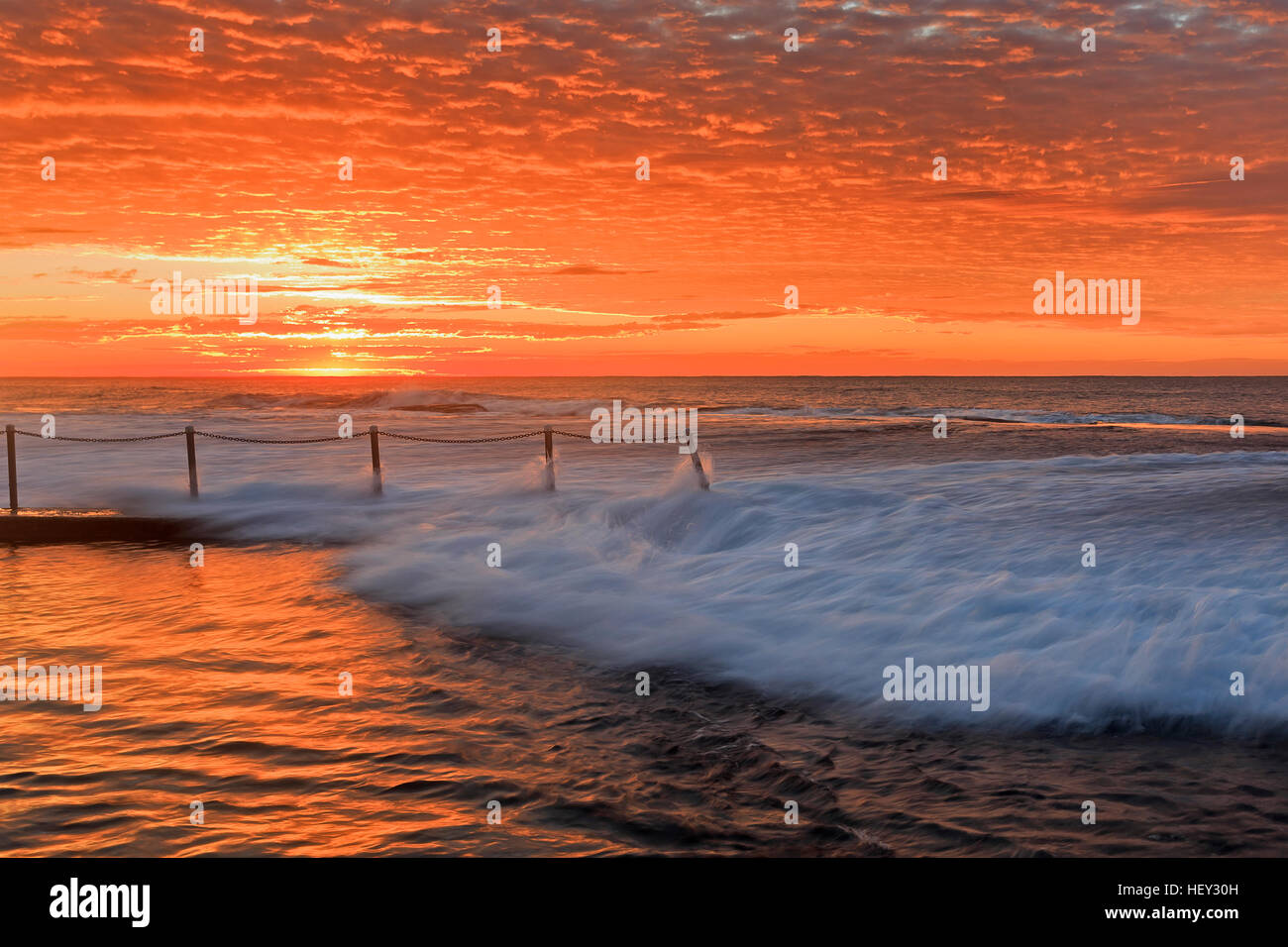 Mona Vale beach rock pool at sunrise. Saturated red sun lights stormy