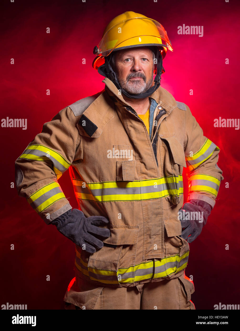 Portrait of a fireman wearing Fire Fighter turnouts and helmet. Background is red and blue smoke and light. Turnouts are protect Stock Photo