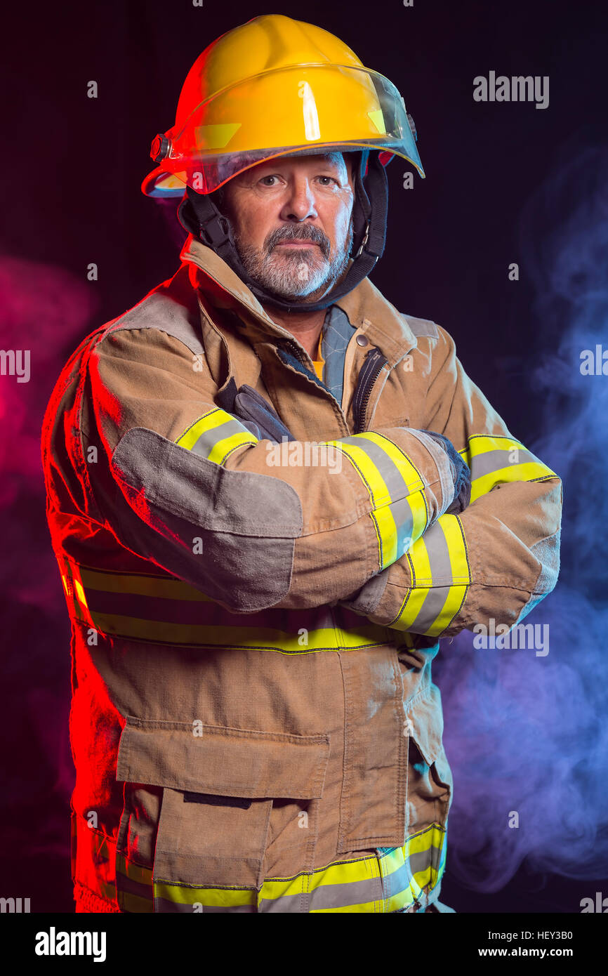 Portrait of a fireman wearing Fire Fighter turnouts and helmet. Background is red and blue smoke and light. Turnouts are protect Stock Photo