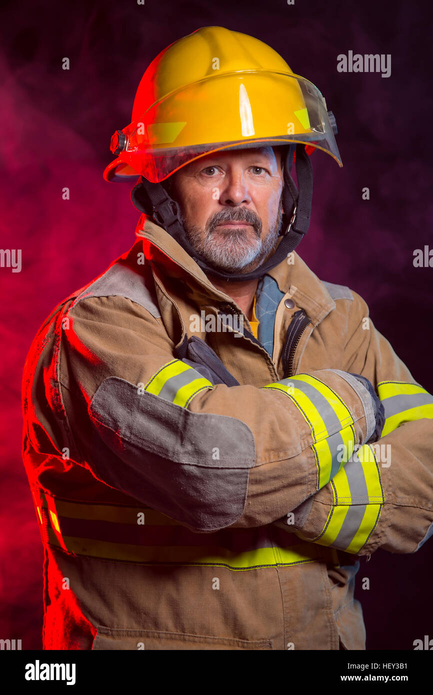 Portrait of a fireman wearing Fire Fighter turnouts and helmet. Background is red and blue smoke and light. Turnouts are protect Stock Photo