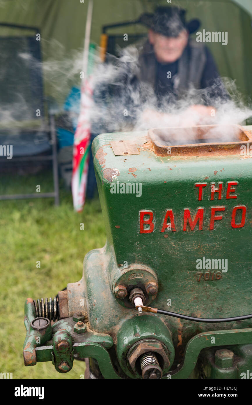 A close up of a Stationary Engine with steam coming out the top at a county show with the owner in the background. Stock Photo