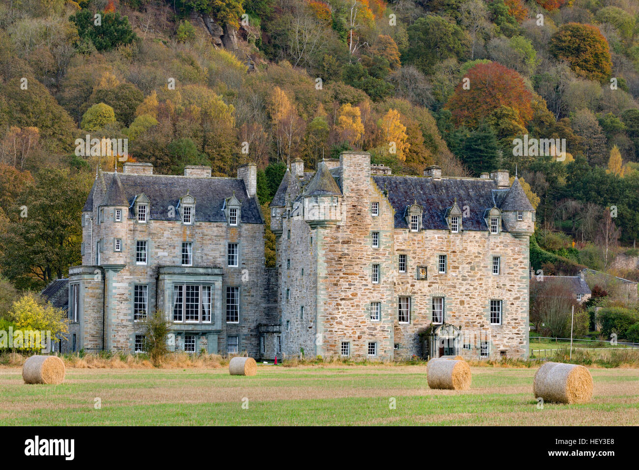 Castle Menzies, Weem, Pertshire, with hay bales in the fireground and a woodland in Autumn colours in the background. Stock Photo