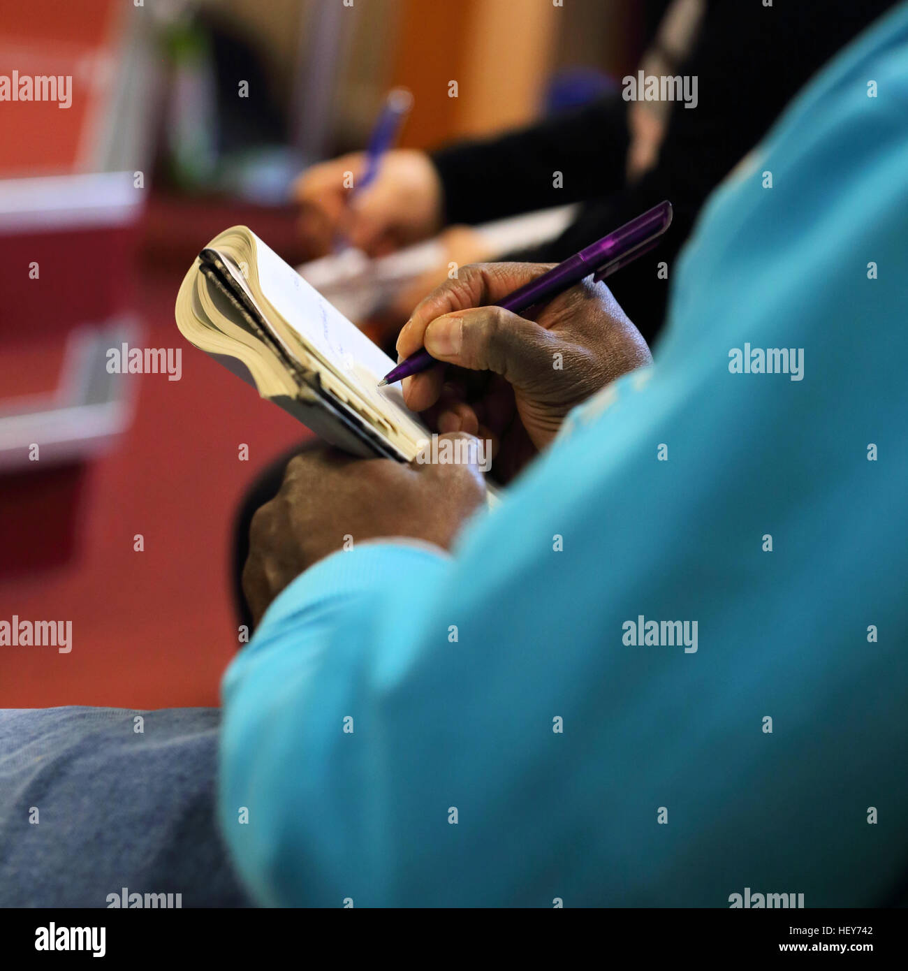 Close-up of a person's hands writing in a notepad during a talk or seminar Stock Photo