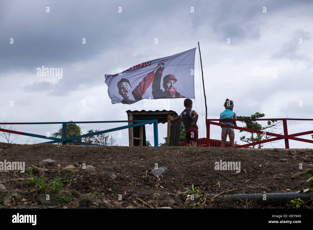 Children and a flag with Fidel and Raul Castro flying at Yomuri, Baracoa, scene of relief efforts, hurricane mathew, Cuba Stock Photo