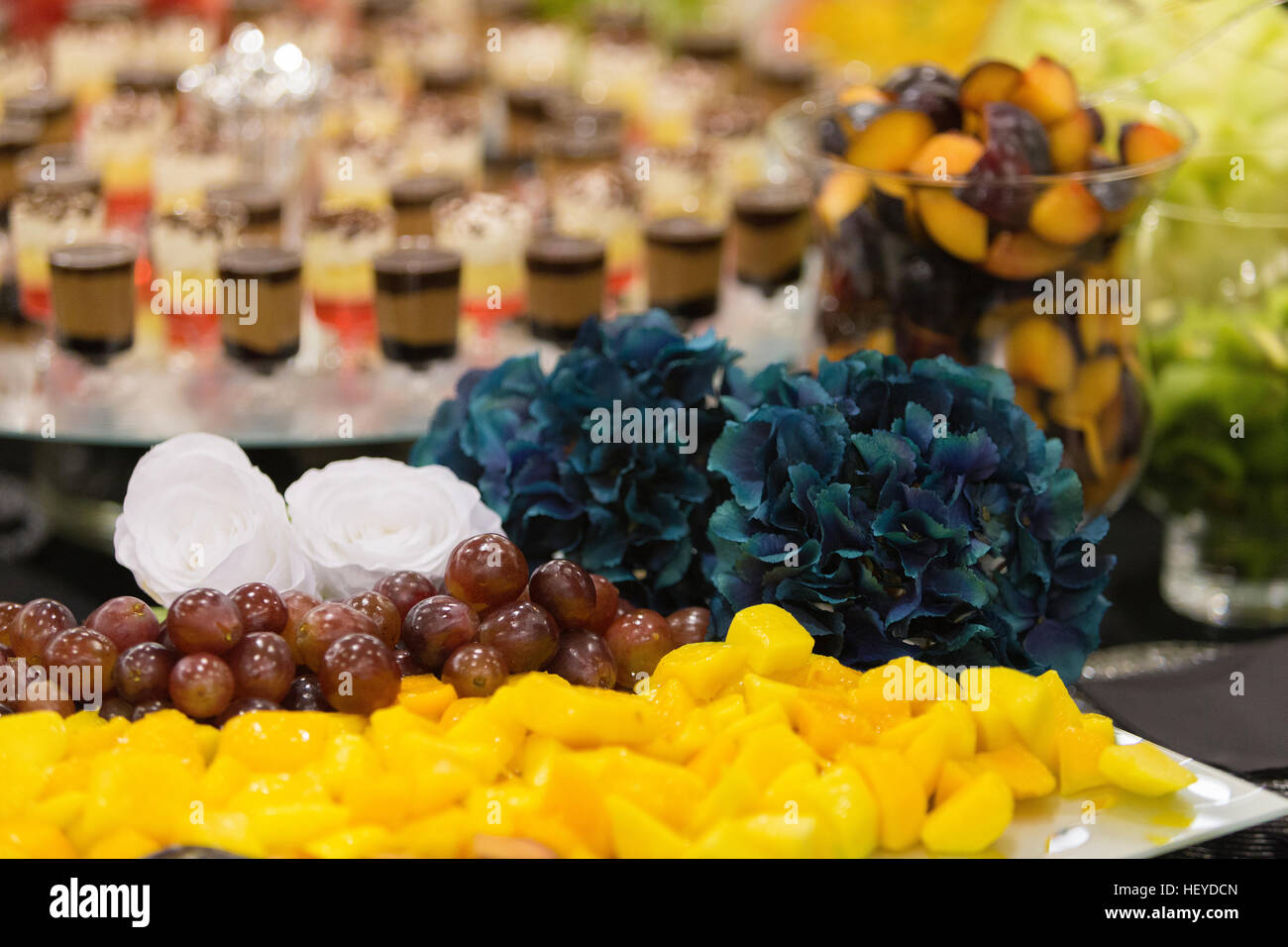 Party buffet of fruit and layered chocolate mousse shots decorated with white roses and blue hydrangeas Stock Photo