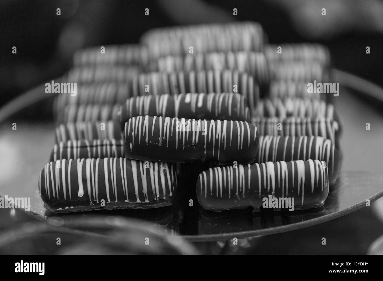 Chocolate fingers drizzled with white icing piled on a plate, monochrome Stock Photo