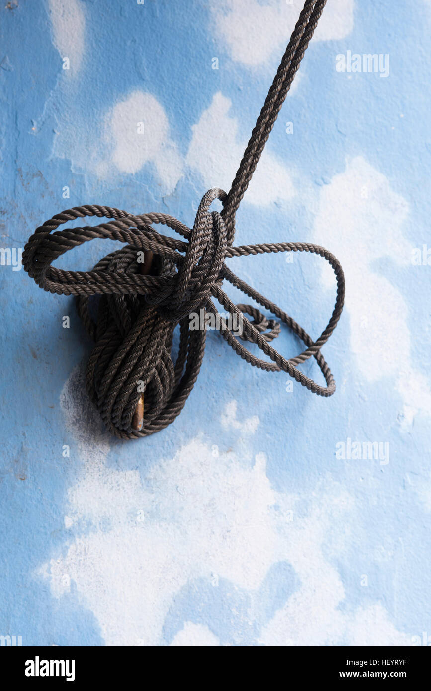 Knotted rope  used for controlling an awning against a pastel blue and white patched wall Stock Photo