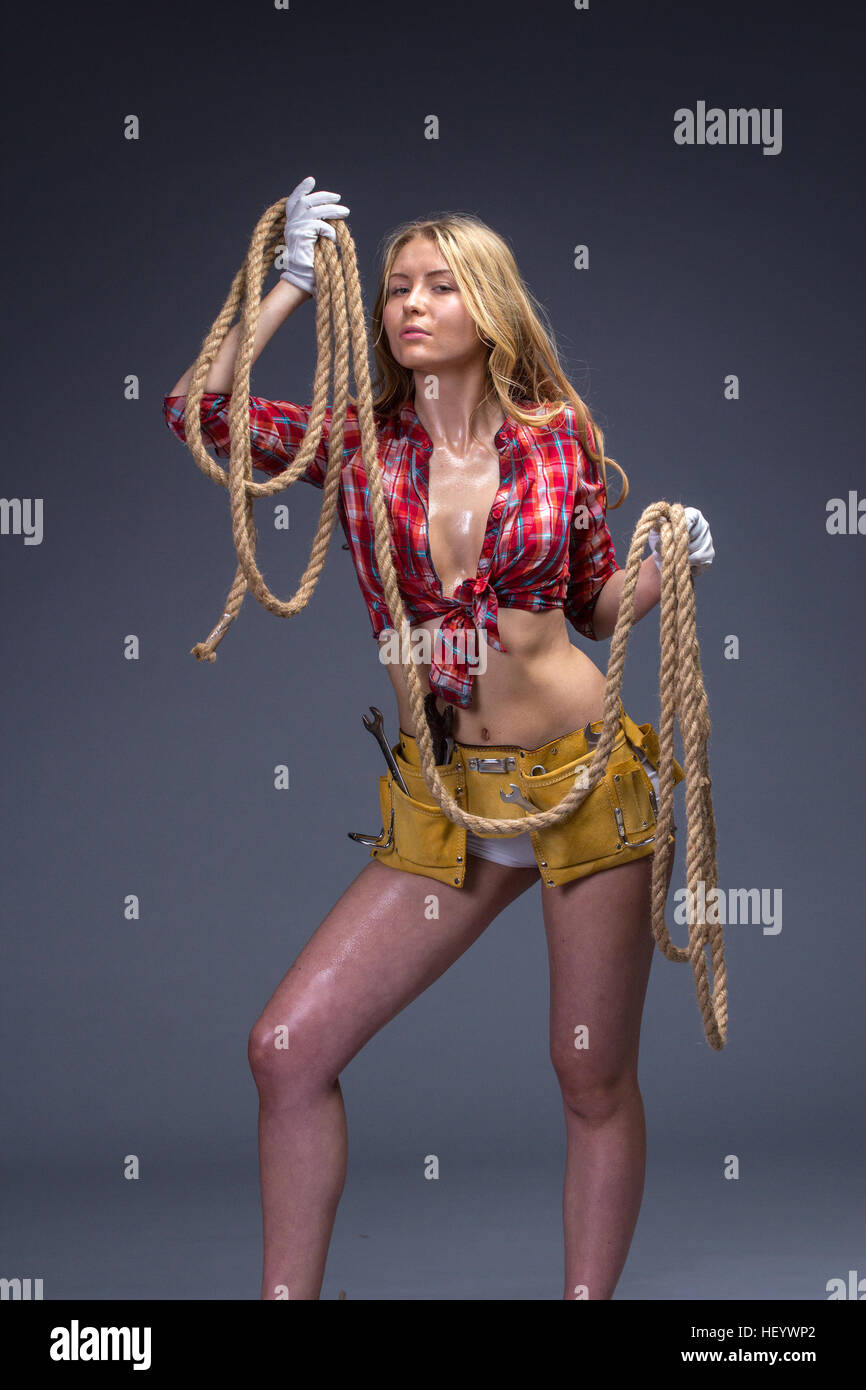 Pretty woman construction worker with tools belt and rope in her hands. Stock Photo