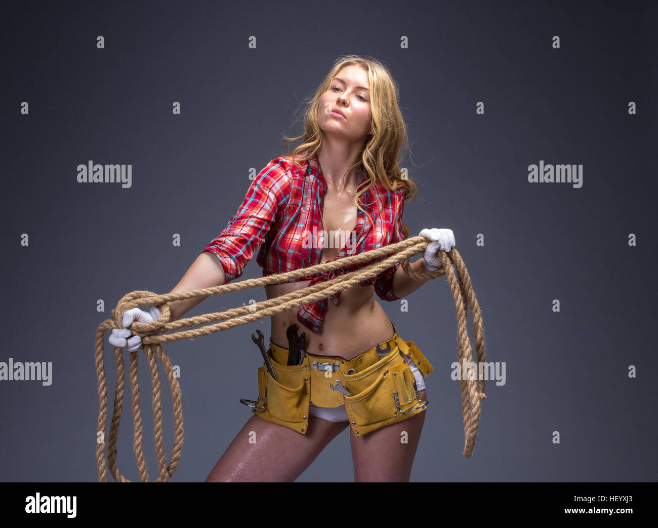 Pretty woman construction worker with tools belt and rope in her hands. Stock Photo