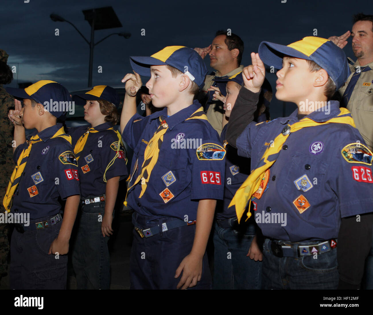 Cub Scouts and den leadership with Wolf Scout Den 3, Pack 625, Poway, Calif., salute the American flag during evening colors ceremony aboard Marine Corps Air Station Miramar, Calif., Nov. 15. When saluting, Cub Scouts and Boy Scouts of all ages stand still and raise their first two fingers to the bill of their hats or edge of the forehead as a sign of respect. Wolf Scouts experience colors aboard Marine air station 121115-M-OB827-038 Stock Photo