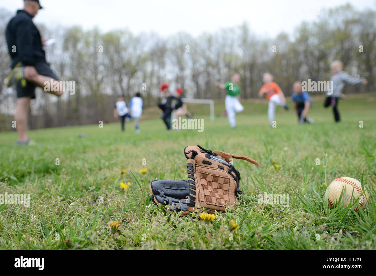 A baseball glove and ball lay upon a field of grass as a Youth Sports' T Ball team warms up