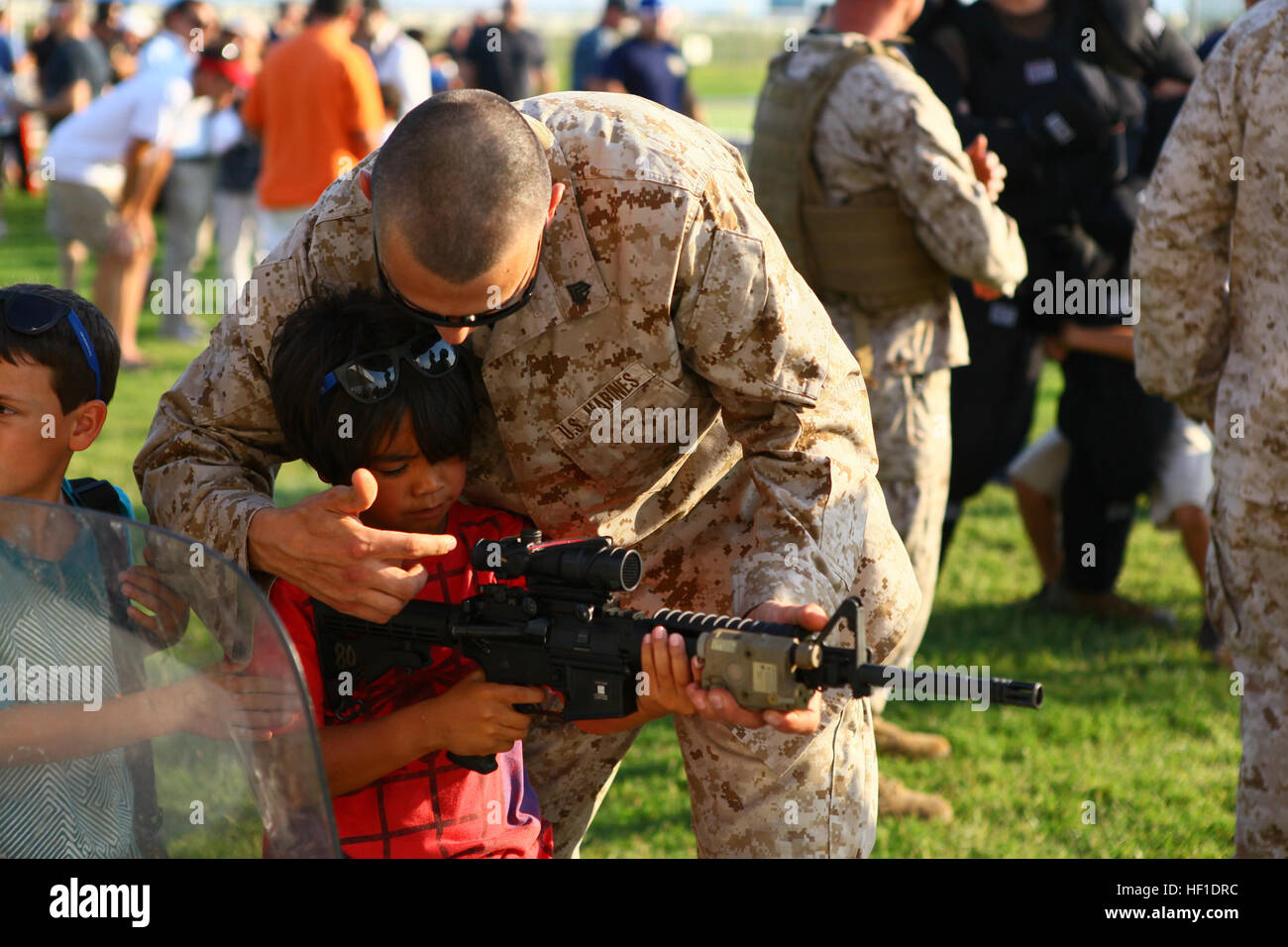 Sgt. Paul Zieniuk, a small arms repair technician with Special-Purpose Marine Air-Ground Task Force Africa 13 shows the rifle combat optics on an M4 to a young boy at the National Night Out aboard Naval Air Station Sigonella, Italy, Aug 6, 2013. Special-Purpose MAGTF Africa participated in the event with a static display of weapons, both lethal and non-lethal. Special-Purpose MAGTF Africa continues to build relationships with the community while simultaneously strengthening U.S. Africa Command and U.S. Marine Corps Forces Africa's ability to assist partner nations in addressing security challe Stock Photo