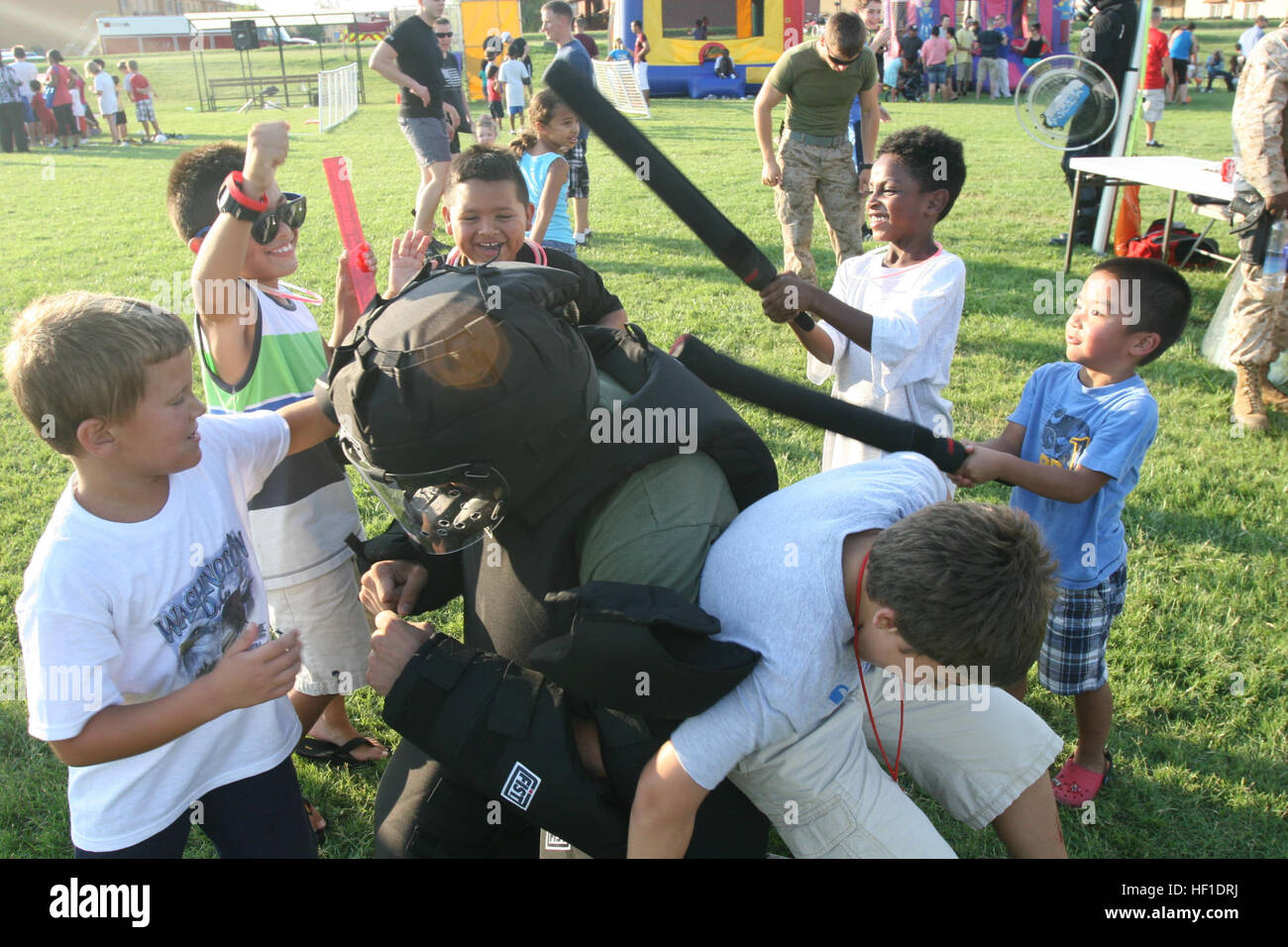Sgt. Paul Zieniuk, a small-arms repairman with Special-Purpose Marine-Air Ground Task Force Africa 13, demonstrates the resilience of riot gear while children strike him with batons at the National Night Out event aboard Naval Air Station Sigonella, Italy, Aug. 6, 2013. Marines and sailors with Special-Purpose MAGTF Africa participated in the event with a static display of weapons, both lethal and non-lethal. Special-Purpose MAGTF Africa continues to build relationships with the community while simultaneously strengthening U.S. Africa Command and U.S. Marine Corps Forces Africa's ability to as Stock Photo
