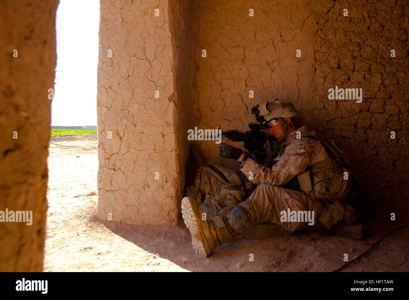 Lance Cpl. Nathan Gulbronson, a Lambertville, Mich., native and rifleman with 1st Battalion, 9th Marines, crouches inside a building while searching for insurgents near the Bari Gul Bazaar, Nad Ali District, Helmand province, Afghanistan, Dec. 4, 2013. Gulbronson posted as security at the far end of a desert compound while his fellow Marines searched the building for lethal aid. Under Fire 131204-M-ZB219-172 Stock Photo